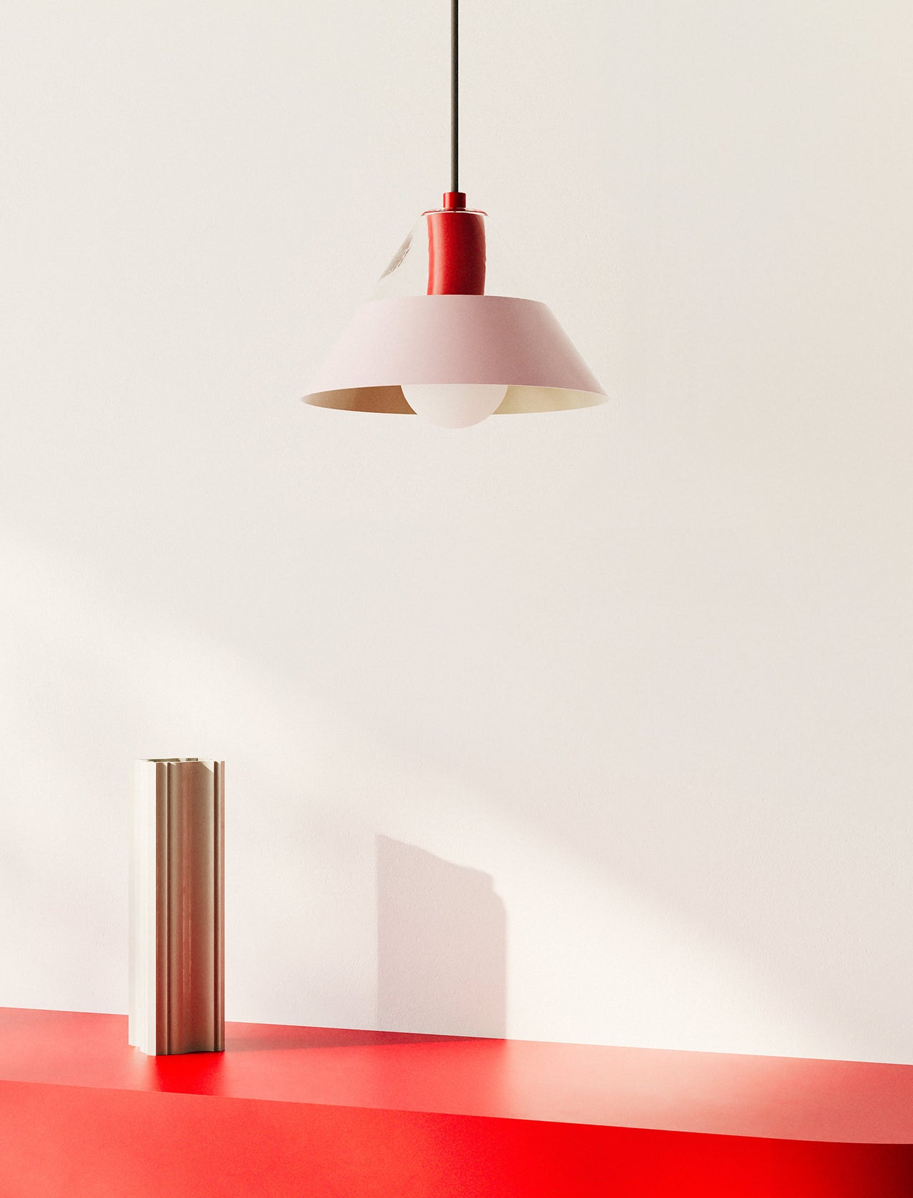 FIFTY FIFTY Lamp with a pink metal shade and red fixture hanging above a red surface and minimalist decor.