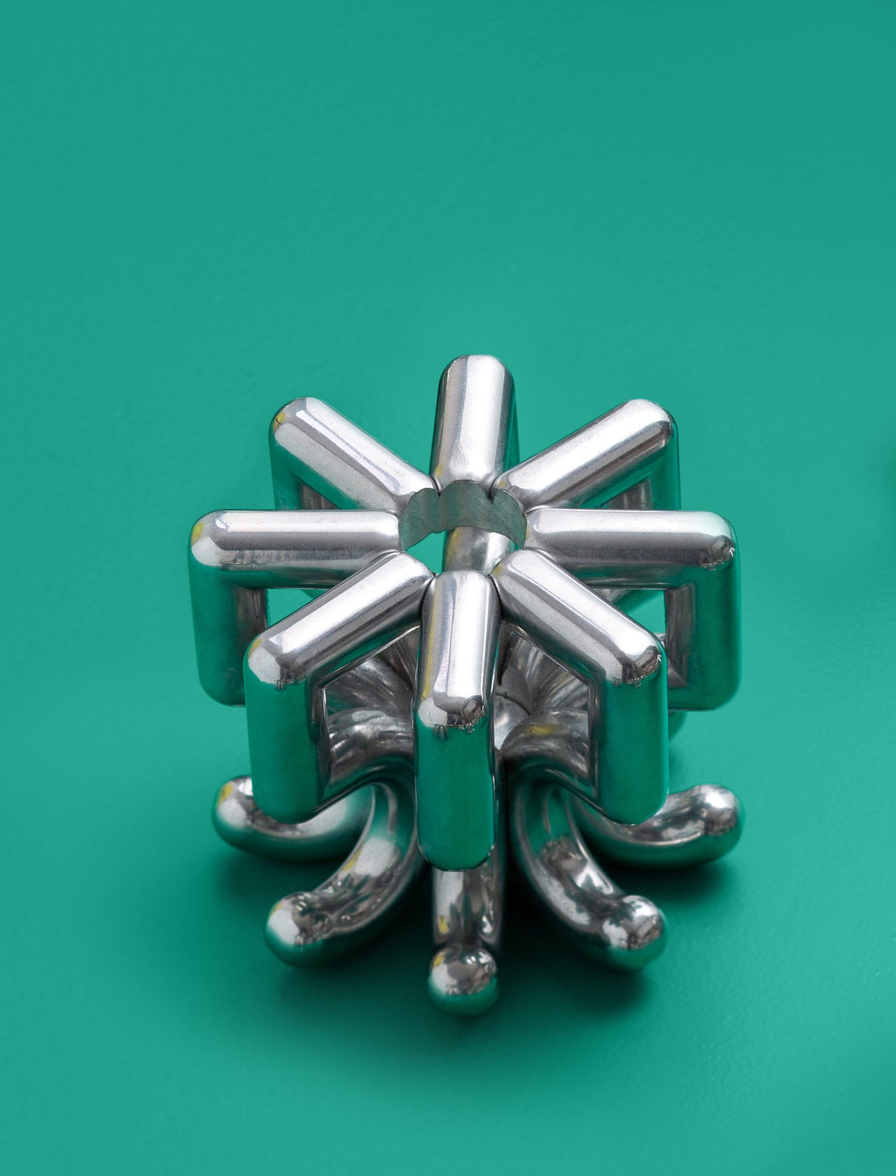 DIGIT FIVE Candlestick made of polished solid aluminum with a modern geometric design on a green background.